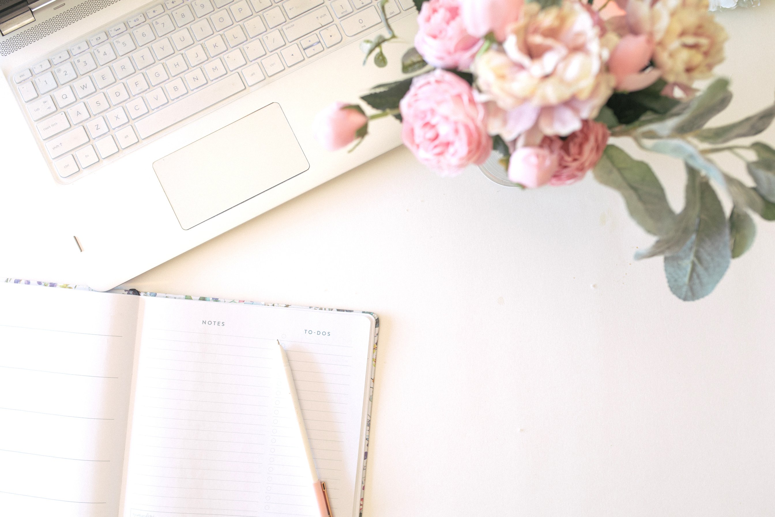 Girl boss working space with laptop, flowers and journal